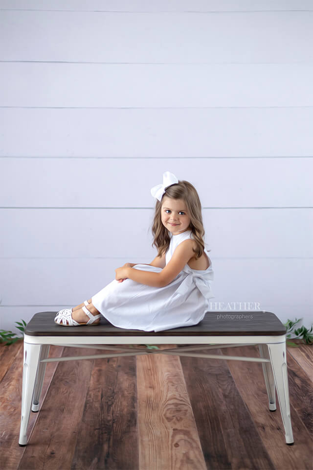 Young girl sitting on vintage bench with shiplap wall