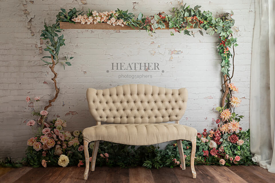 A cozy living room scene with a comfortable, neutral-colored couch positioned in front of a rustic brick wall. A vibrant bouquet of flowers rests on the armrest, adding a touch of color to the space.