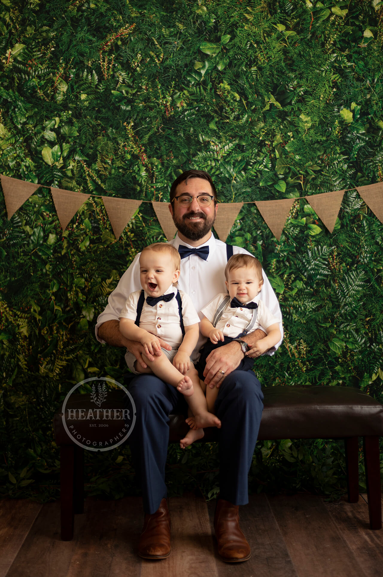 man holding two babies against floral backdrop